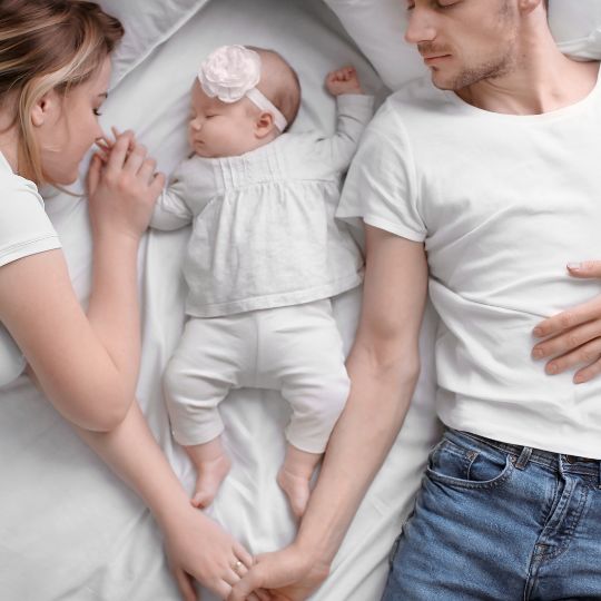 mom dad and baby sleeping in bed stock