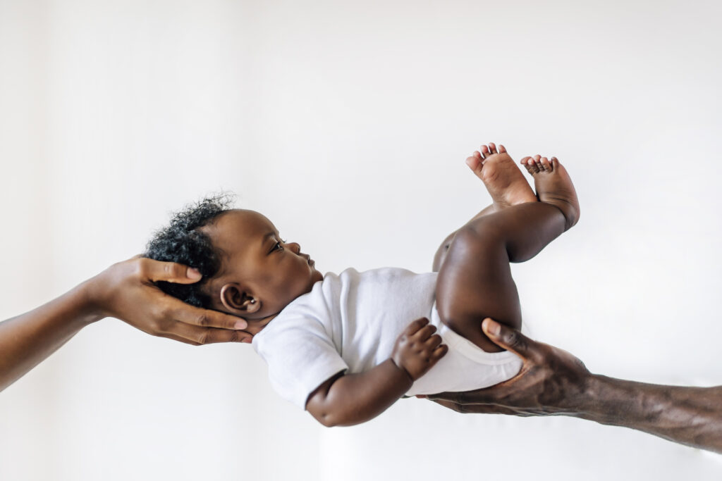 An African-American baby being held up in the air by her parents against a white wall