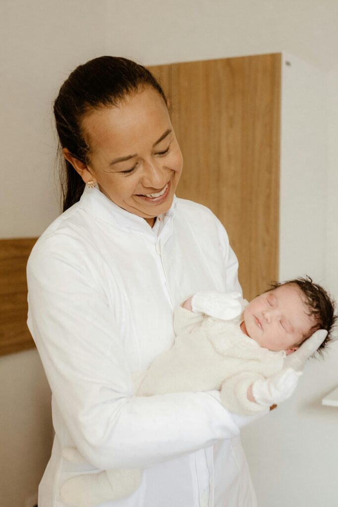 A compassionate Newborn Care Specialist holding a sleeping newborn while providing physician-led newborn care, feeding support, and postpartum guidance in the family's home.