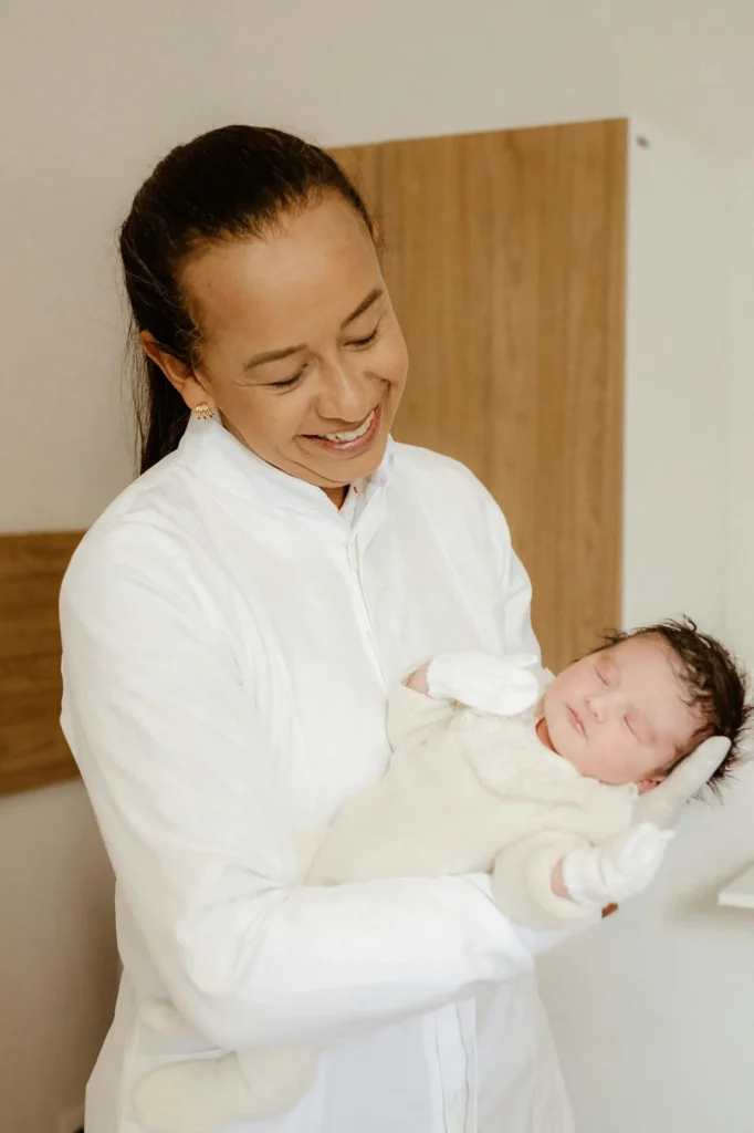 A compassionate Newborn Care Specialist holding a sleeping newborn while providing physician-led newborn care, feeding support, and postpartum guidance in the family's home.